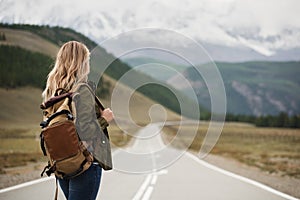 A woman with a backpack and a road stretching into the distance