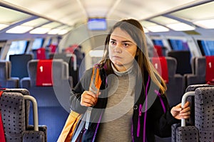 Woman with backpack on shoulder standing in aisle between seats in train