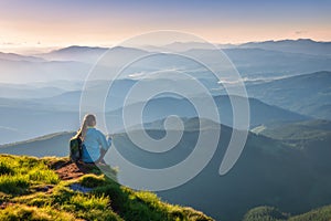 Woman with backpack sitting on the mountain peak at sunset