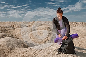 Woman with backpack sitting on one knee on yellow dunes on sunny day