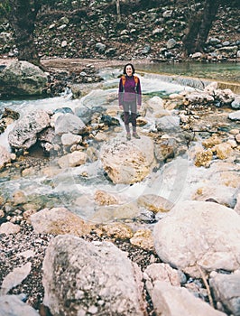 A woman with a backpack is standing near a mountain river