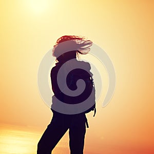 Woman with backpack standing on sunrise windy coast