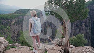 A woman with a backpack stands on the edge of a cliff in the canyon and looks into the distance. Tara Canyon in Turkey.