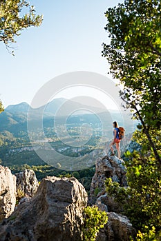 A woman with a backpack stands on top of a mountain and admires the beauty of a mountain valley