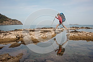 Woman with backpack treks on sea coast