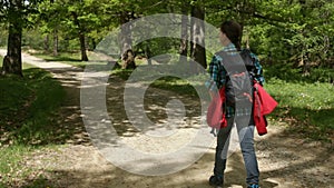 Woman with backpack walking on a dusty road in the forest