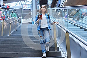 Woman with backpack walking up the stairs near escalator in modern station building