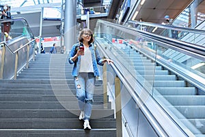 Woman with backpack walking up the stairs near escalator in modern station building