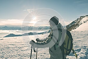 Woman backpacker with hiking poles looking at view high up on the Alps. Rear view, winter cold snow, sun star in backlight, split