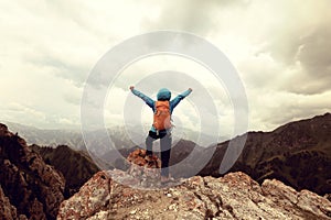 Woman backpacker open arms on mountain peak