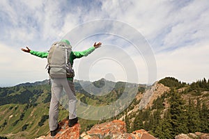 Woman backpacker open arms on mountain peak