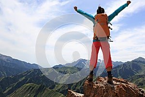 woman backpacker open arms on mountain peak cliff