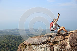 Woman backpacker taking photo with cellphone on mountain peak