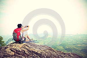 Woman backpacker taking photo with cellphone on mountain peak