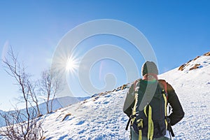 Woman backpacker trekking on snow on the Alps. Rear view, winter lifestyle, cold feeling, sun star in backlight.