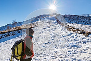 Woman backpacker trekking on snow on the Alps. Rear view, winter lifestyle, cold feeling, sun star in backlight.