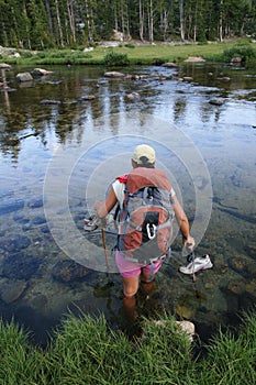 Woman backpacker wading across river