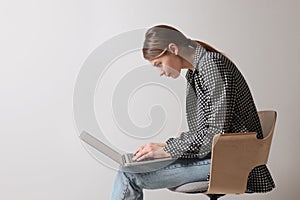 Woman with bad posture using laptop while sitting on chair against light grey background, space for text