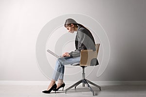 Woman with bad posture using laptop while sitting on chair near light grey wall indoors