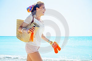 Woman with bag, flip flops and bottle of sunscreen running