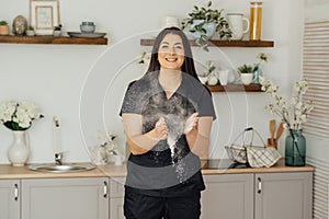 Woman baker clapping and sprinkling white flour over dough on kitchen background