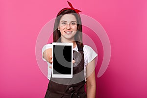 Woman, baker wears brown apron dirty with flour, showing blank empty screen with copy space. Happy Caucasian model poses smiling