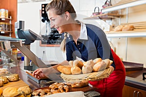 Woman in bakery shop putting bread into display to sell it
