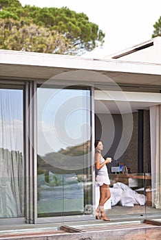 Woman, balcony and bedroom with coffee on pajamas in morning, fresh and healthy at home in Los Angeles. Glass door
