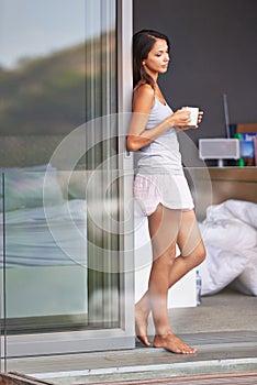 Woman, balcony and bedroom in morning with coffee on pajamas, fresh air and healthy at home in Los Angeles. Glass door