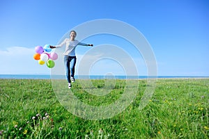 Woman with balloons jumping on green grassland