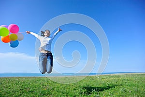 Woman with balloons jumping on green grassland