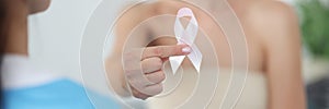 Woman with bandaged chest holding pink ribbon at doctor appointment closeup