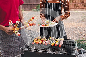 A woman with a barbecue plate and a man grilling barbecue and pork in dinner party. Food, people and family time concept