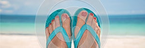 Woman bare sandy feet with blue flip flops, beach in the background