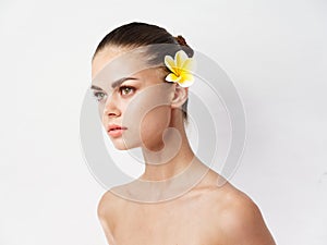 woman with bare shoulders cosmetics flower behind ear cropped view light background