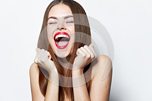 Woman with bare shoulders laughs with his mouth wide open and hands near his face lipstick