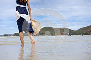 Woman barefoot hold hat and walking on summer along wave of sea water and sand on the beach