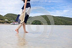 Woman barefoot hold hat and walking on summer along wave of sea water and sand on the beach
