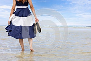 Woman barefoot hold her shoes walking on summer along wave of sea water and sand on the beach