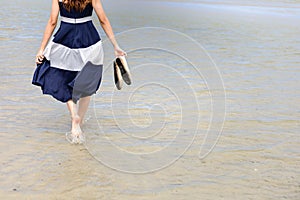 Woman barefoot hold her shoes walking on summer along wave of sea water and sand on the beach