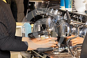 The woman barista prepares coffee in a coffee machine and pours it into paper cups