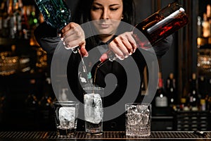 Woman bartender gently pours drink from bottle to glass with ice.