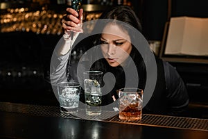 Woman bartender gently pours drink to glass with ice.