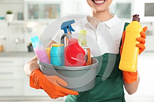 Woman with basin of detergents and bottle in kitchen. Cleaning service