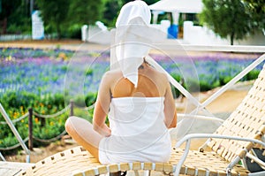 A woman in a bath towel is sitting on a lounge on a terrace