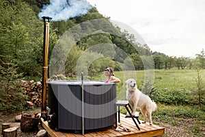 Woman bathing in hot tube, while resting with her dog on nature