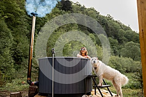 Woman bathing in hot tube, while resting with her dog on nature