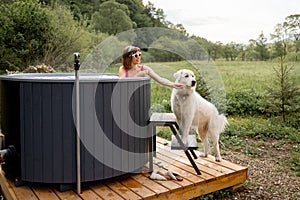 Woman bathing in hot tube, while resting with her dog on nature