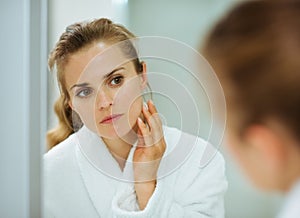 Woman in bathrobe checking her face in mirror