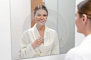 Woman in bathrobe looking in mirror at bathroom